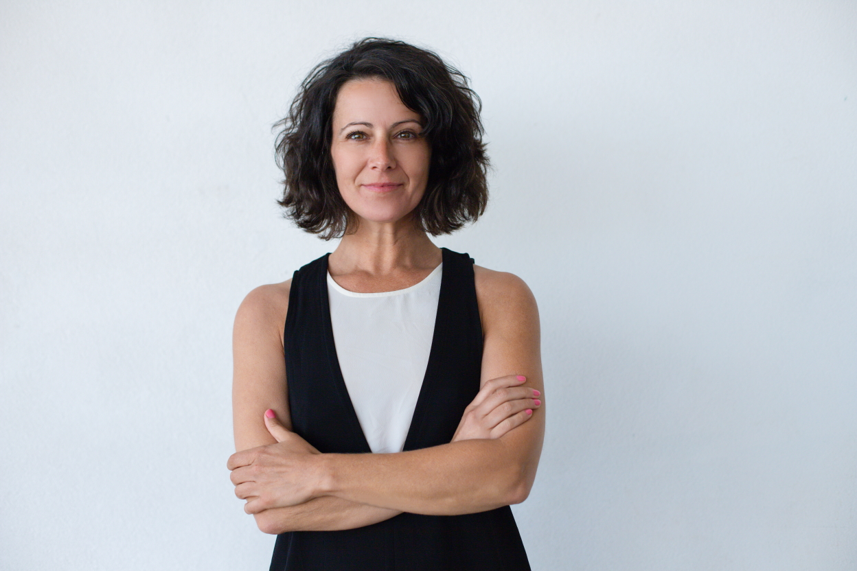 Highly Sensitives and the Benefits of Naturally Recognizing Patternsattractive brunette woman standing with crossed arms and smiling at camera isolated on grey background. Emotion concept